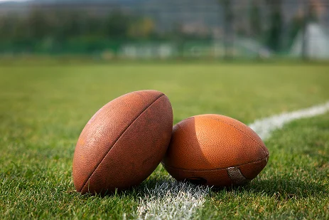 Duas bolas de futebol americano colocadas na relva verde perto de uma linha de campo ao ar livre